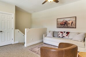 A living room with a beige carpet, a brown leather chair, a white sofa with decorative pillows, a painting of horses on the wall, and a ceiling fan. - Community Perks! Modern PHX Condo: Extended Stay! (Phoenix)