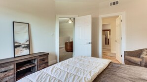 Un dormitorio con cama, cómoda, silla y puerta que da a otra habitación.