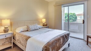 Un dormitorio con cama, mesitas de noche, ventilador de techo y puerta corrediza de vidrio a un balcón.