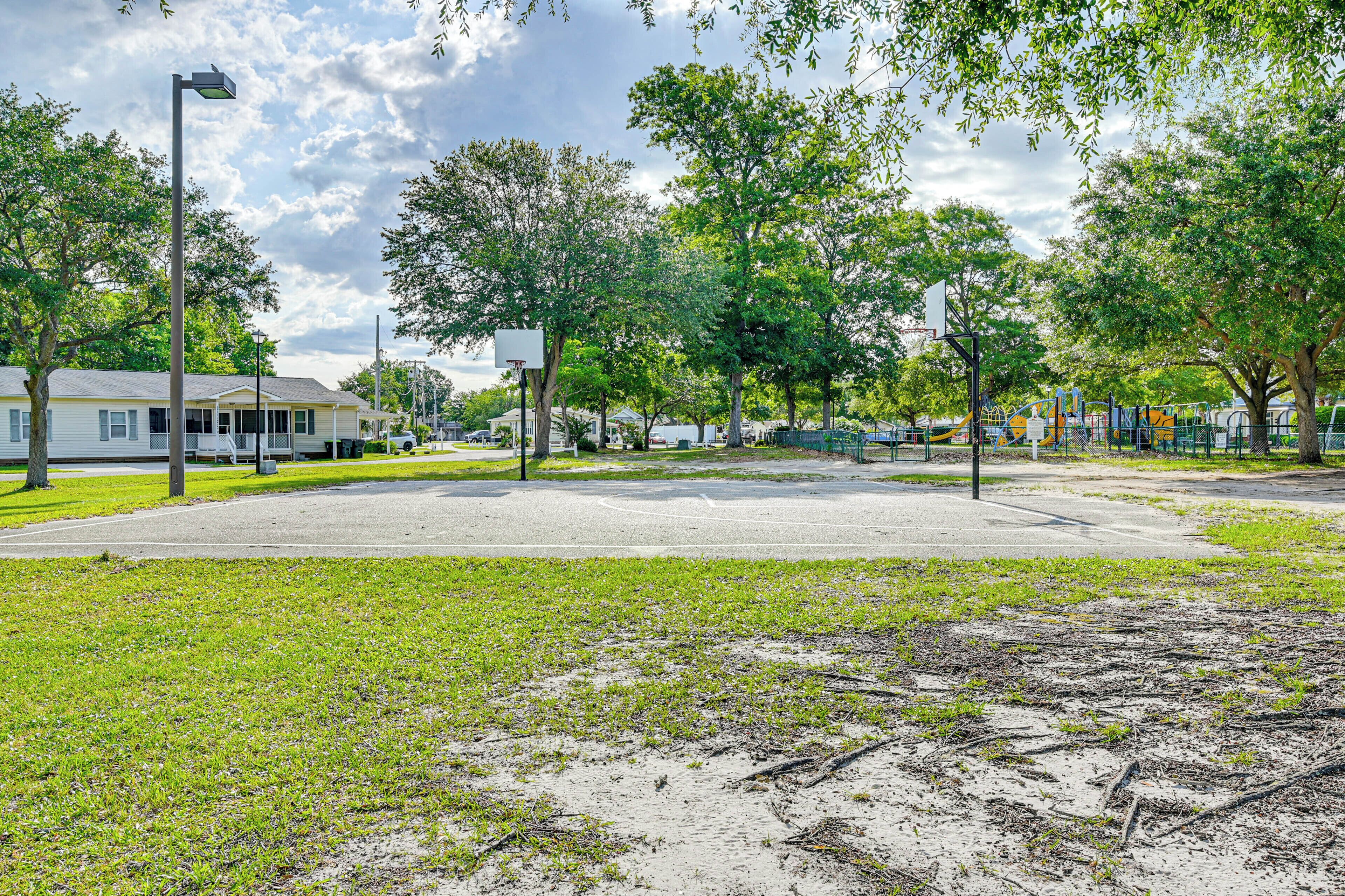 A park with playground equipment, a basketball court, and a street with houses.