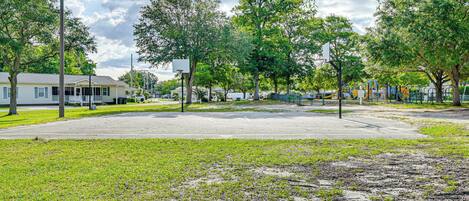 A park with playground equipment, a basketball court, and a street with houses.