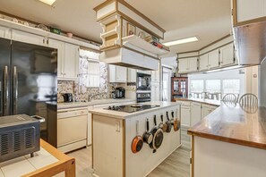 Eine Küche mit weißen Schränken, einem Edelstahl-Kühlschrank, einem eingebauten Backofen und einer Kochinsel mit hängenden Töpfen.