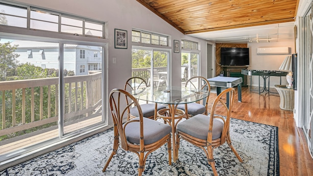 A dining area with a glass table and wicker chairs, a television, and a kitchen area with a grill. - < 1 Mi to Sand! Family-friendly Surfside Beach Gem (Murrells Inlet)