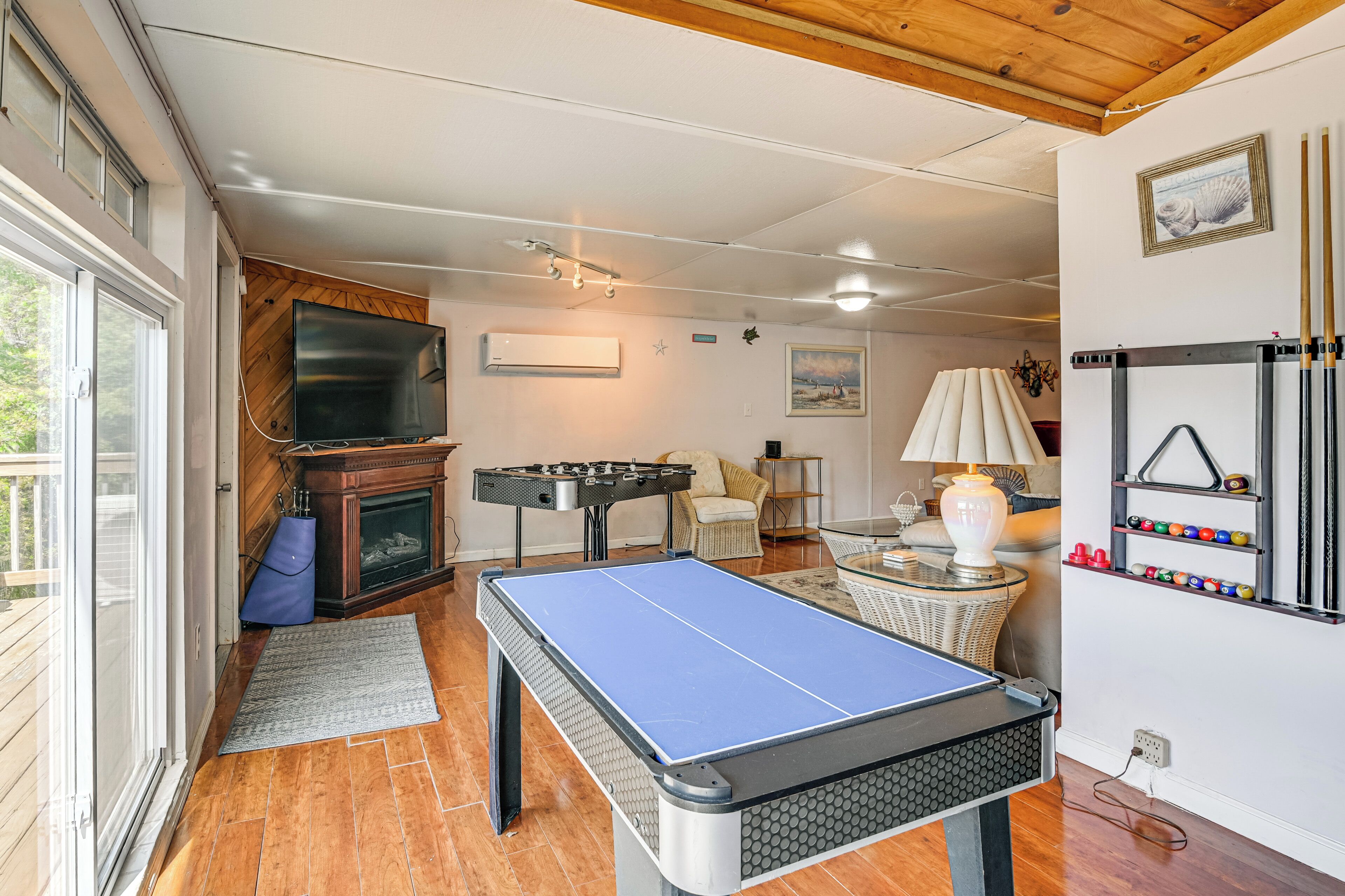 A room with a ping pong table, a foosball table, a fireplace, and a billiards rack.