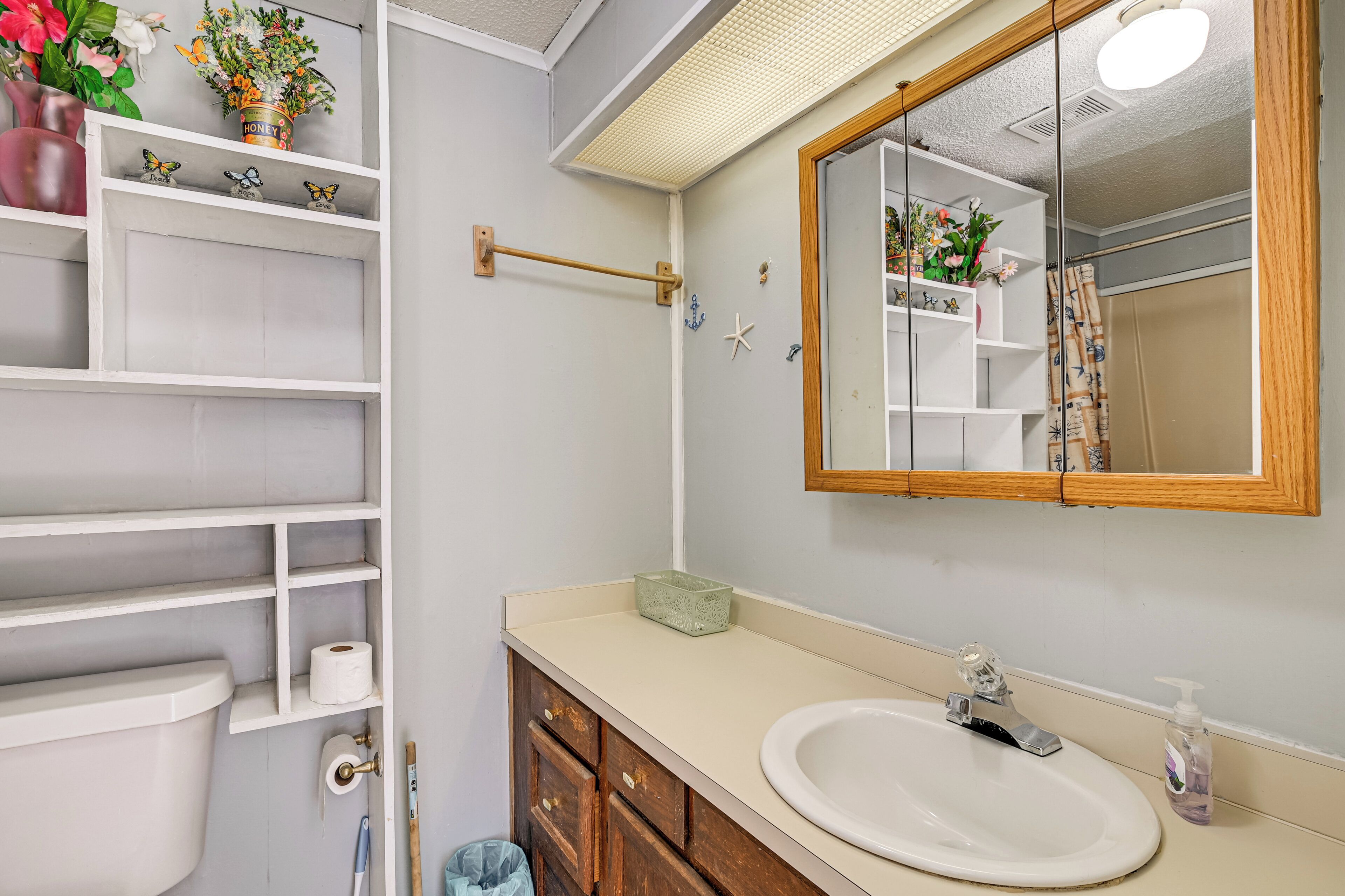 A bathroom with a toilet, sink, mirror, shelves with toiletries, and a shower curtain.
