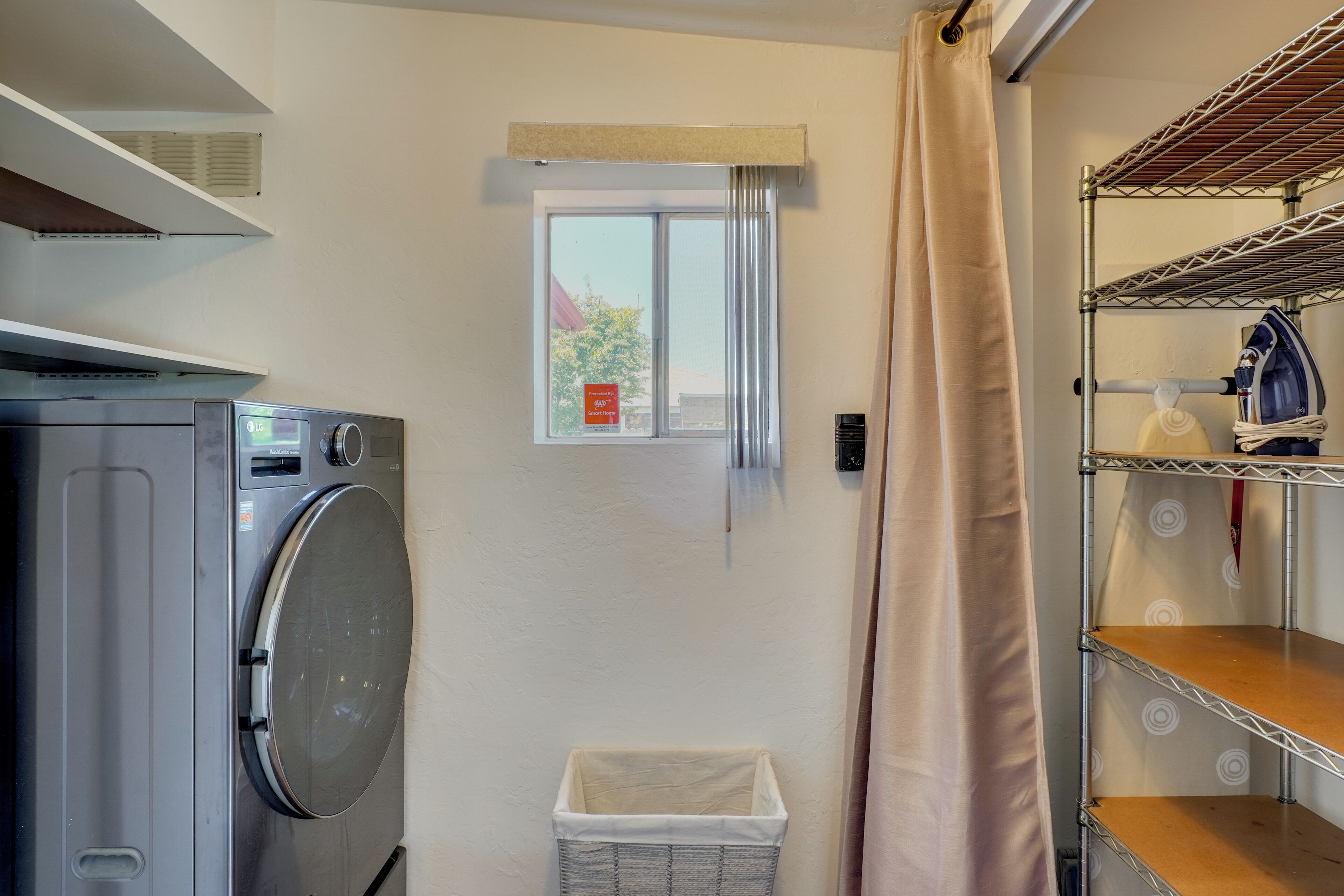 A laundry area with a washing machine, a drying rack, a small window, and a storage shelf.