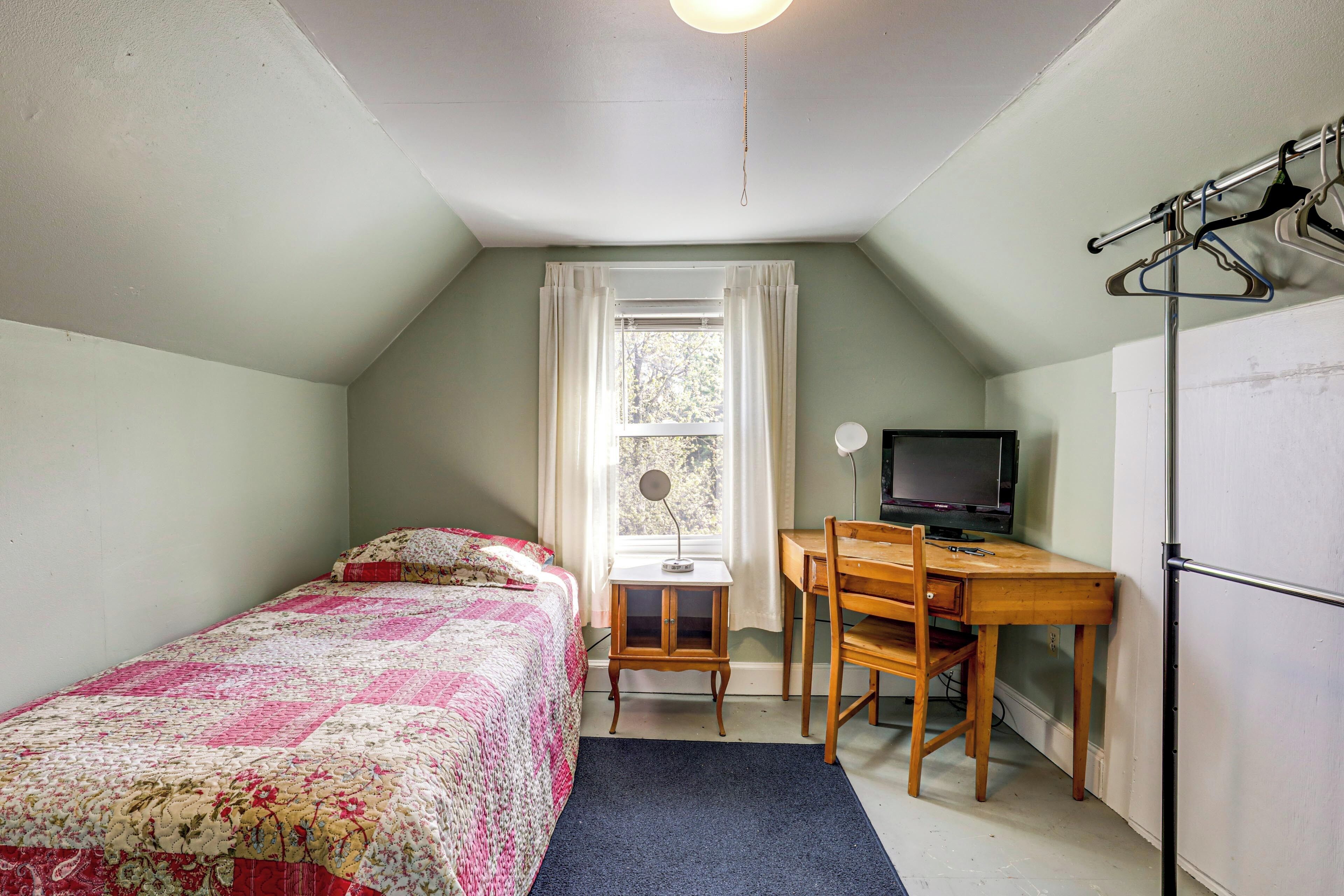 Ein Schlafzimmer mit einem Bett, einem Schreibtisch, einem Stuhl, einem Fernseher und einem Fenster.