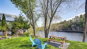 A picnic area with a table and chairs by a lake, surrounded by trees and a building in the background. - Near Trails & Lakes! Pemigewasset River Townhome (Franklin)
