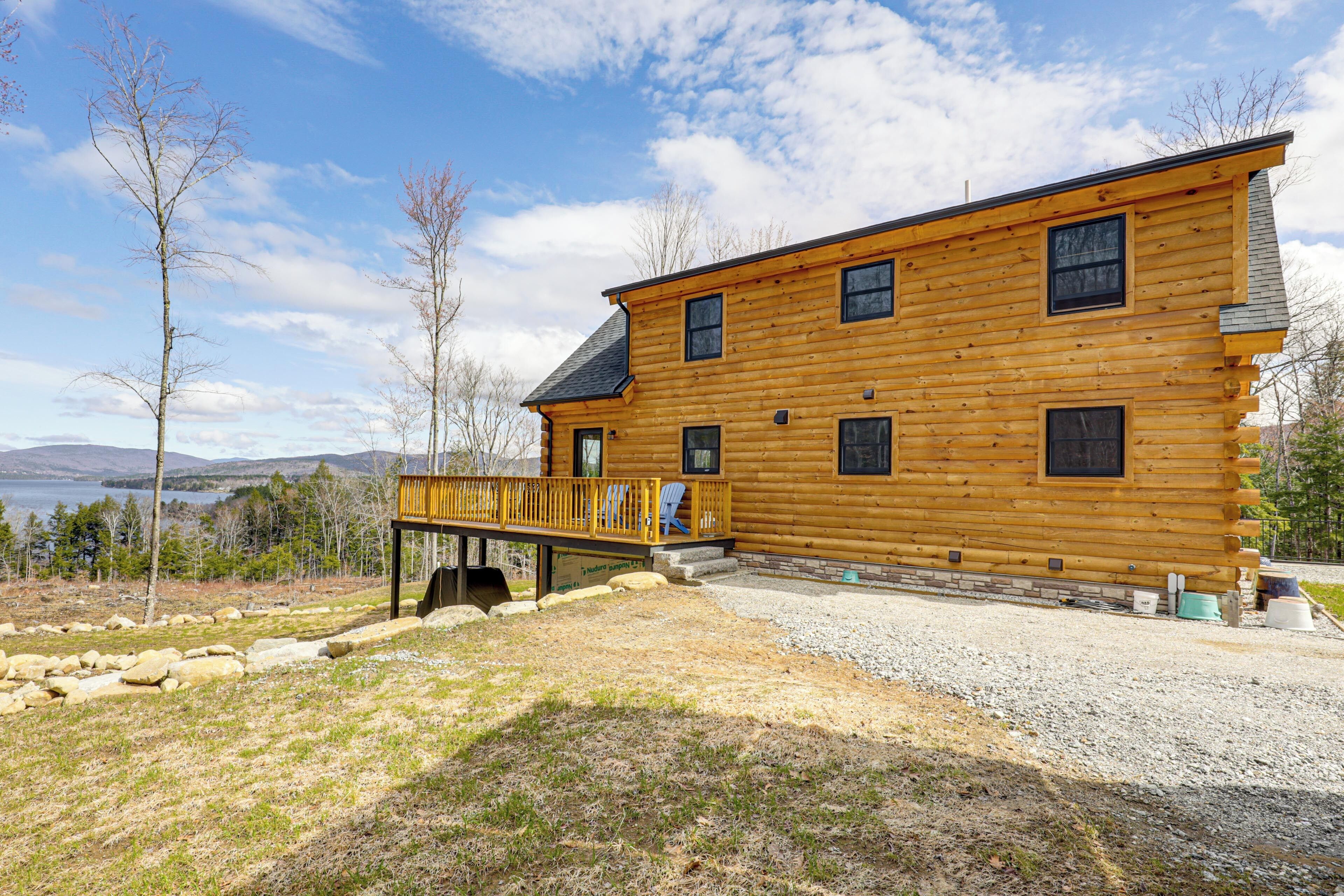 A log cabin with a deck, multiple windows, and a view of a lake and mountains.