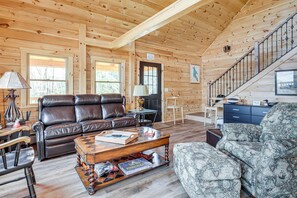 A wooden cabin interior with a leather sofa, patterned armchair, and a staircase. - Newfound Lake Getaway: Cabin w/ Deck, Fire Pit (Bristol)