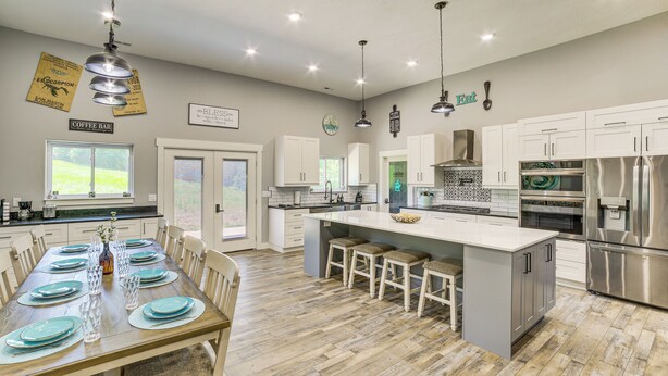 A modern kitchen with a central island, stainless steel appliances, and a dining area with a wooden table and chairs. - Spacious Barndominium Near Branson w/ Game Rooms (Omaha)