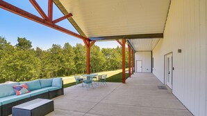 An outdoor covered patio with a sofa, chairs, and a table. - Spacious Barndominium Near Branson w/ Game Rooms (Omaha)