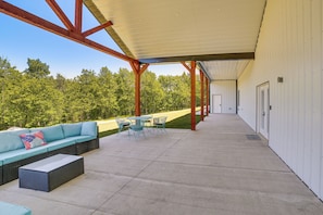 An outdoor covered patio with a sofa, chairs, and a table. - Spacious Barndominium Near Branson w/ Game Rooms (Omaha)
