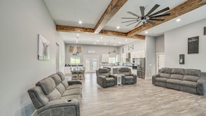 A spacious living area with a modern ceiling fan, a dining table, and a kitchen in the background. - Spacious Barndominium Near Branson w/ Game Rooms (Omaha)