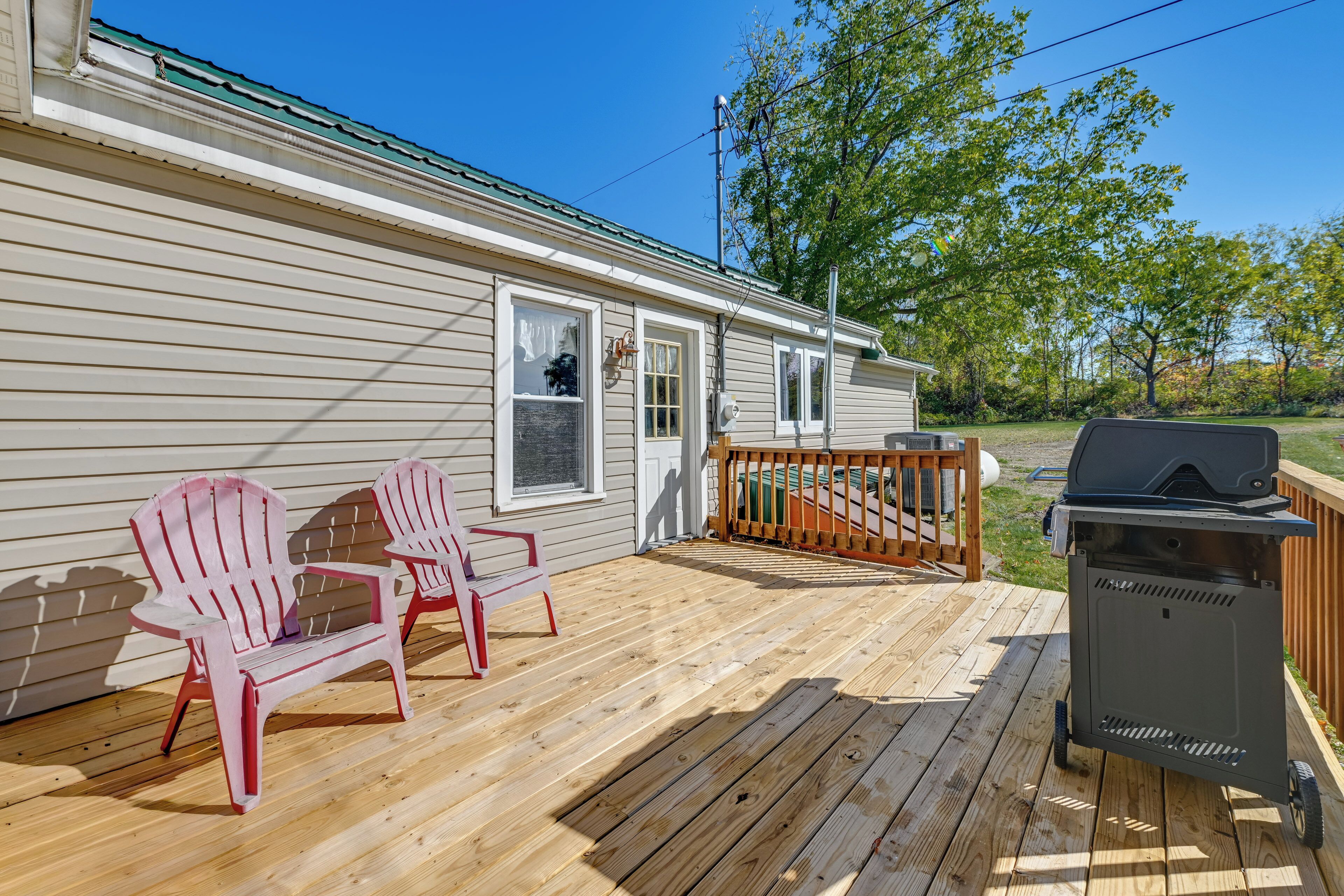 Una terraza de madera con dos sillas Adirondack, una parrilla y una casa con techo verde.