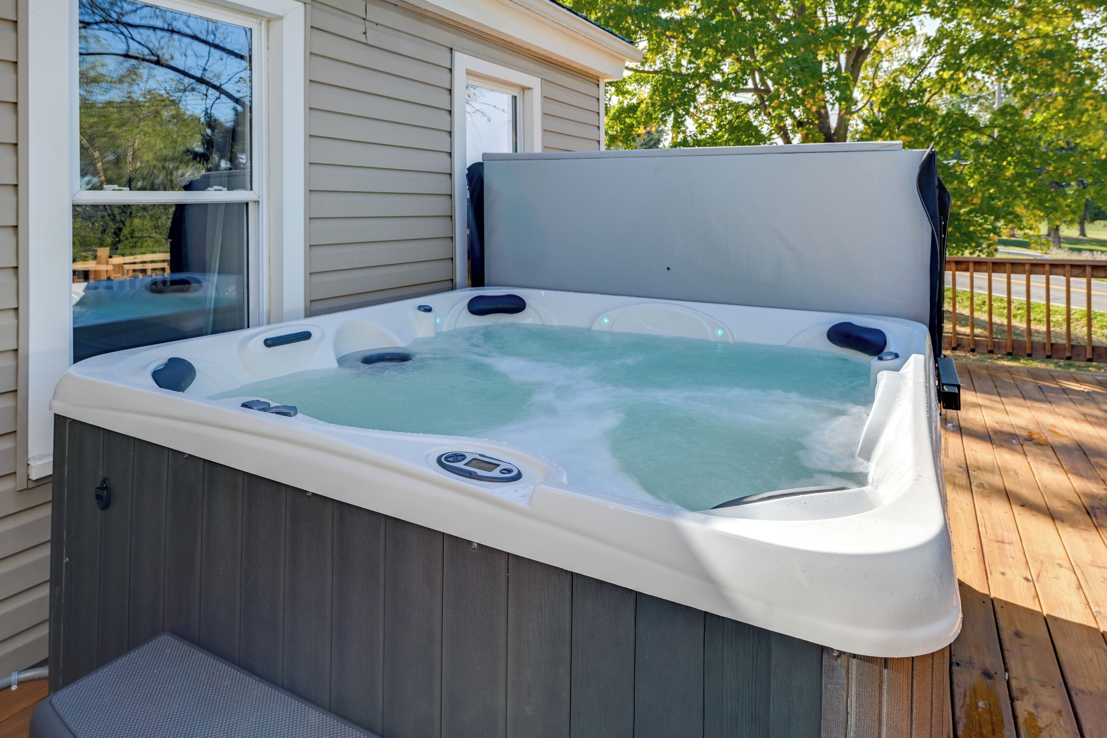 A hot tub on a wooden deck with a house in the background.