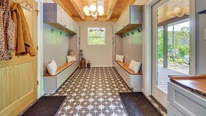 A hallway with a patterned floor, wooden ceiling beams, and a window with a view of greenery.