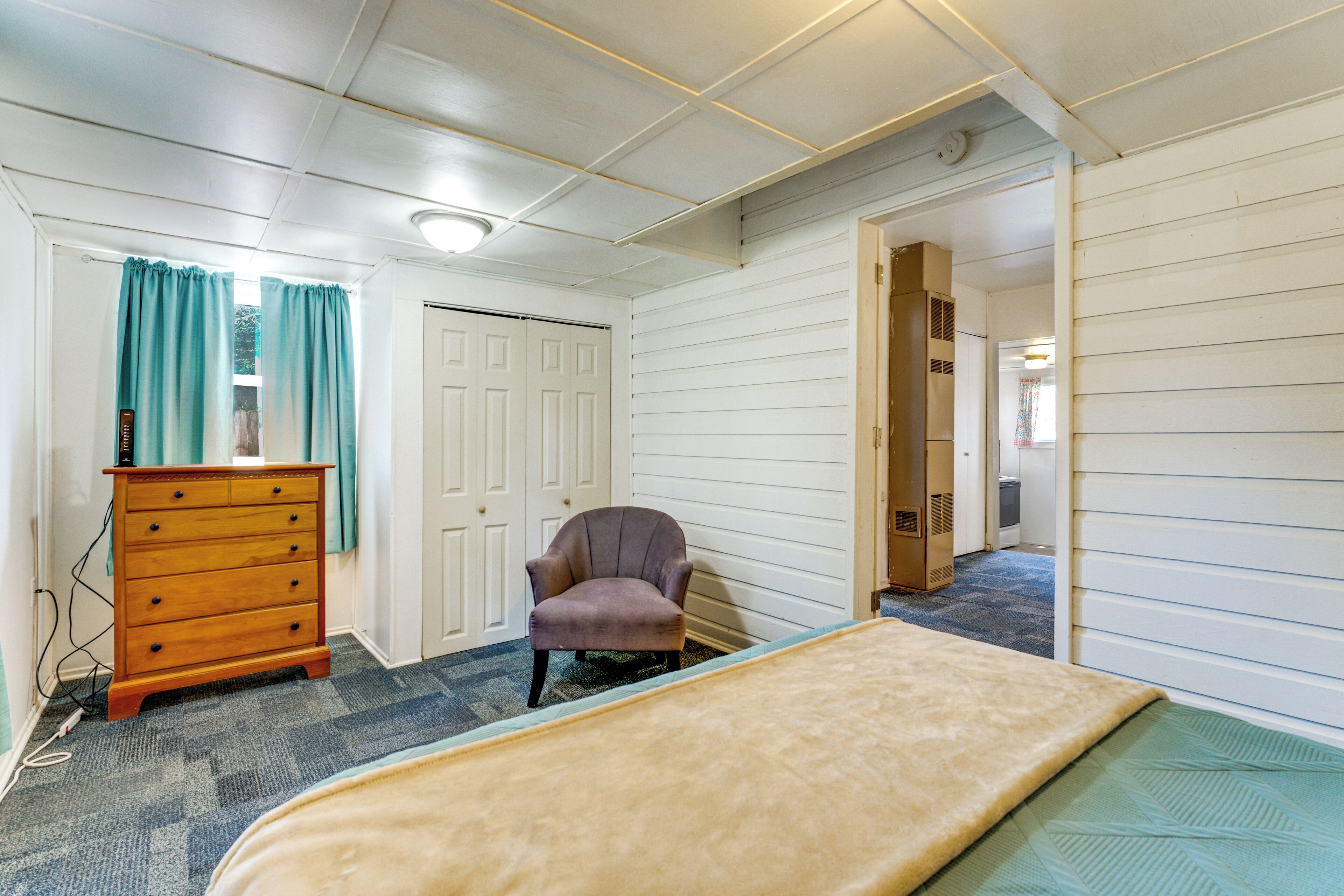 Une pièce comprenant un lit, une commode, une chaise et une porte donnant sur une autre pièce.