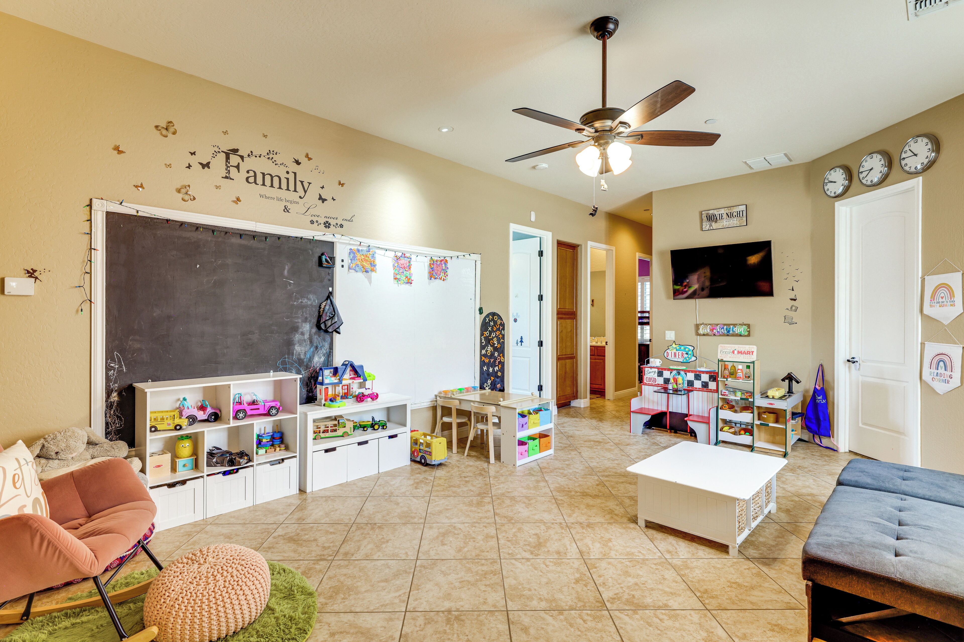 Une pièce bien éclairée, dotée d’un ventilateur de plafond, d’un tableau blanc et de divers jouets et matériels pédagogiques pour enfants.