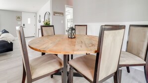 A round wooden dining table with six chairs, a mirror, and a hanging light fixture in a modern room with a door and a bench in the background. - Walk to Yacht Club! Devils Lake Escape (Manitou Beach)