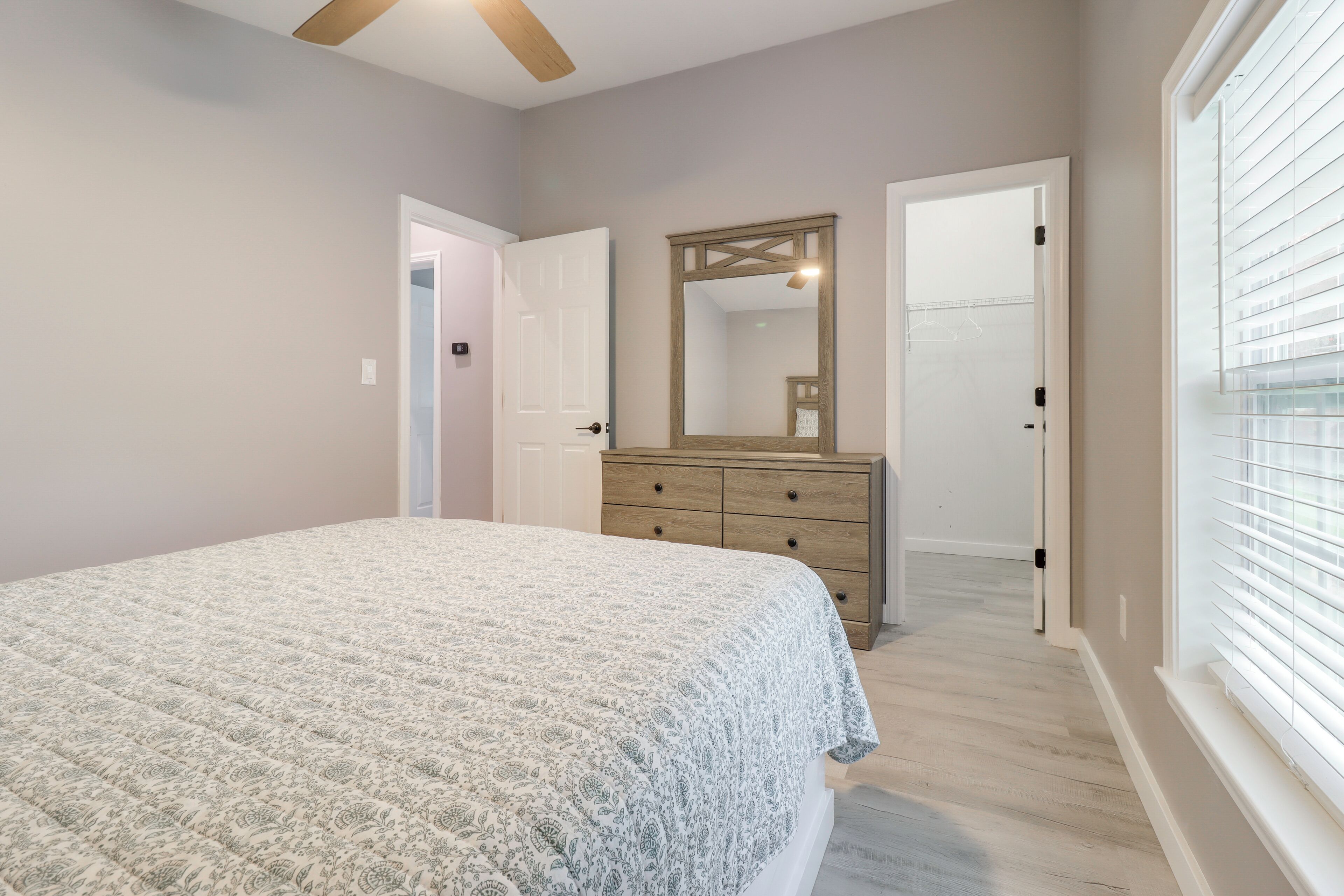 A bedroom with a bed, dresser, mirror, and a door leading to another room.
