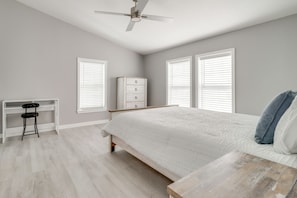 A bedroom with a bed, a desk, a dresser, and a ceiling fan.