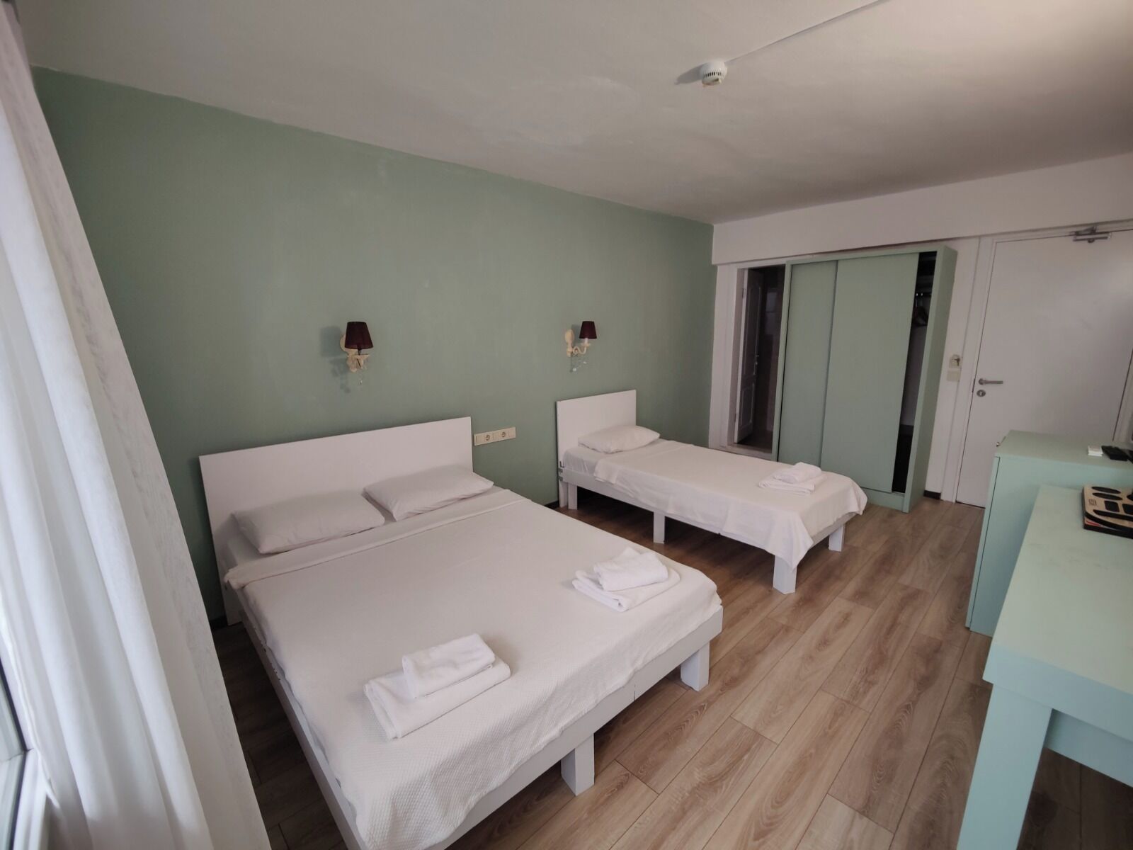 A hotel room with two single beds, a desk, a wardrobe, and a door leading to a bathroom.