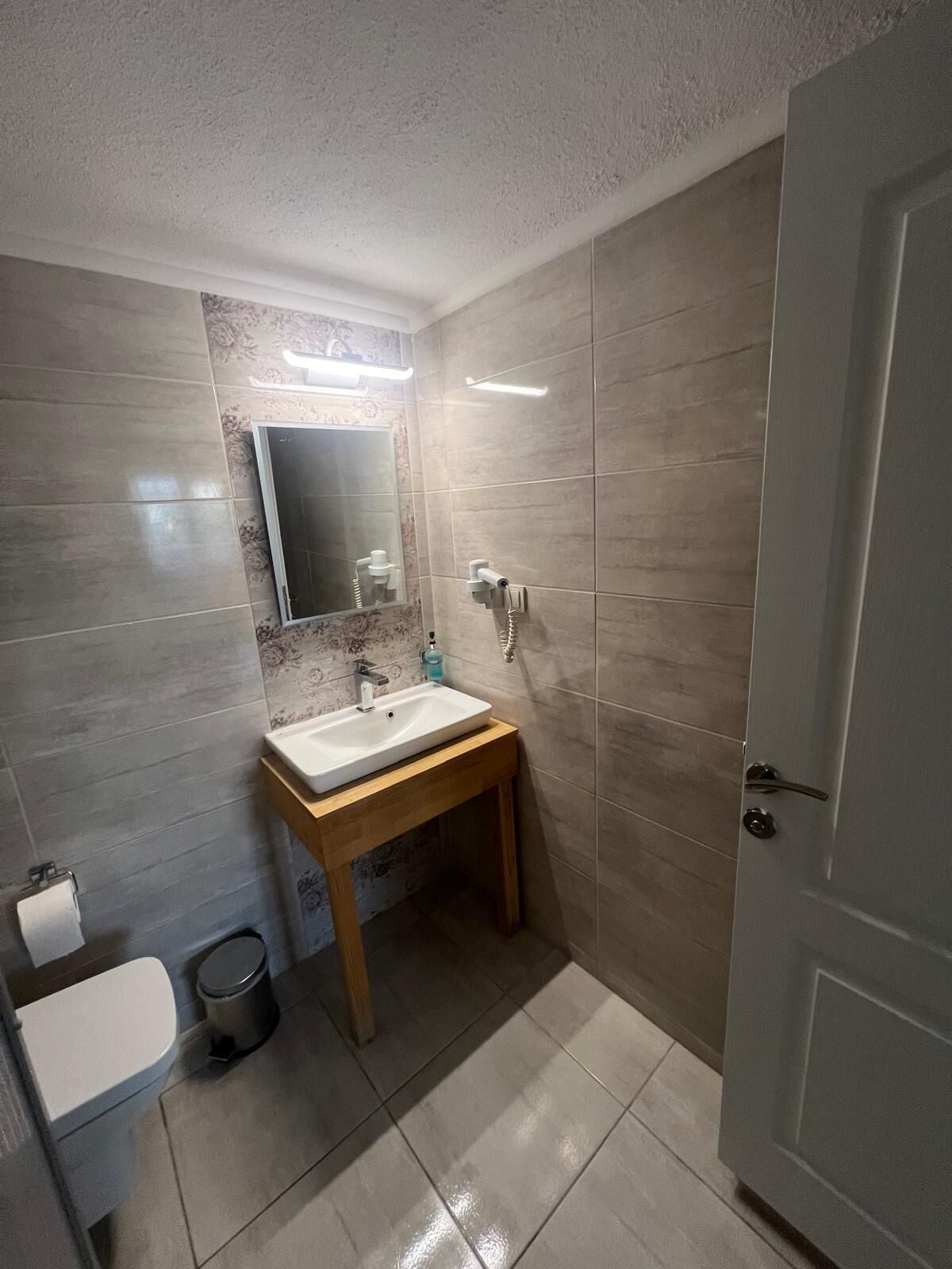 A bathroom with a sink, mirror, toilet, and a door.