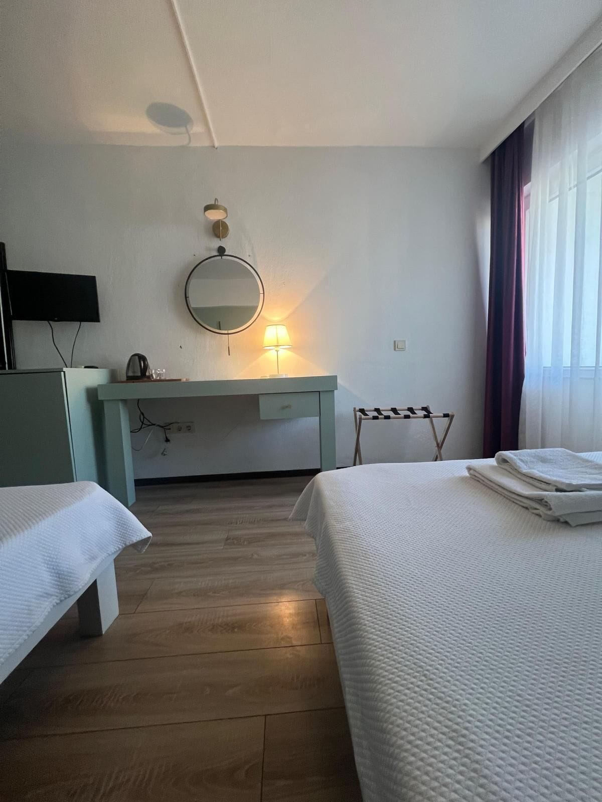 A hotel room with two beds, a desk with a lamp, a mirror, and a TV mounted on the wall.