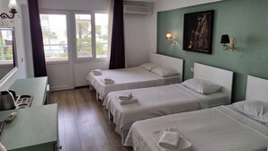 A hotel room with two beds, a desk, a window with curtains, an air conditioning unit, and a painting on the wall.