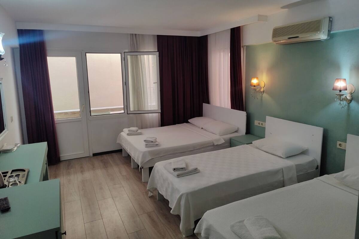 A hotel room with two beds, a desk, a window, and an air conditioning unit.