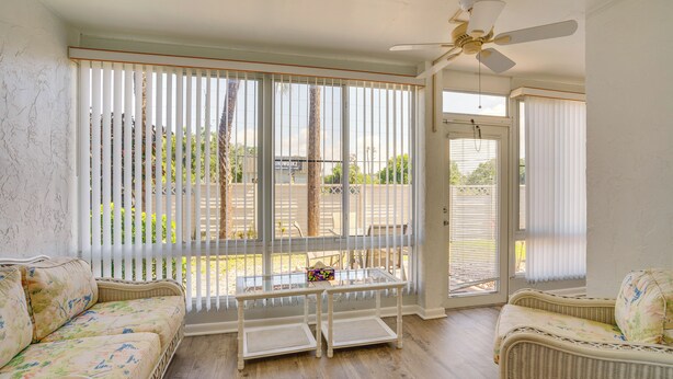 A room with a wicker sofa, a small table, a ceiling fan, and large windows with blinds. - 2 Mi to Sand! Port Charlotte Condo w/ Pool Access (Punta Gorda)