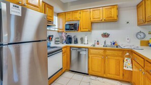 A kitchen with wooden cabinets, a stainless steel refrigerator, a microwave, and a dishwasher. - 2 Mi to Sand! Port Charlotte Condo w/ Pool Access (Punta Gorda)