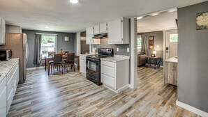 A modern kitchen with white cabinetry, a built-in oven, and a dining area with a table and chairs. - Lake Tawakoni Basecamp: Covered Patio + Fire Pit! (Wills Point)