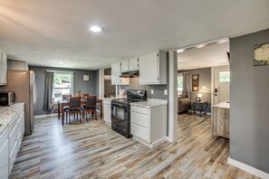 A modern kitchen with white cabinetry, a built-in oven, and a dining area with a table and chairs. - Lake Tawakoni Basecamp: Covered Patio + Fire Pit! (Wills Point)