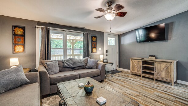 A living room with a sofa, coffee table, and a TV mounted on the wall. - Lake Tawakoni Basecamp: Covered Patio + Fire Pit! (Wills Point)