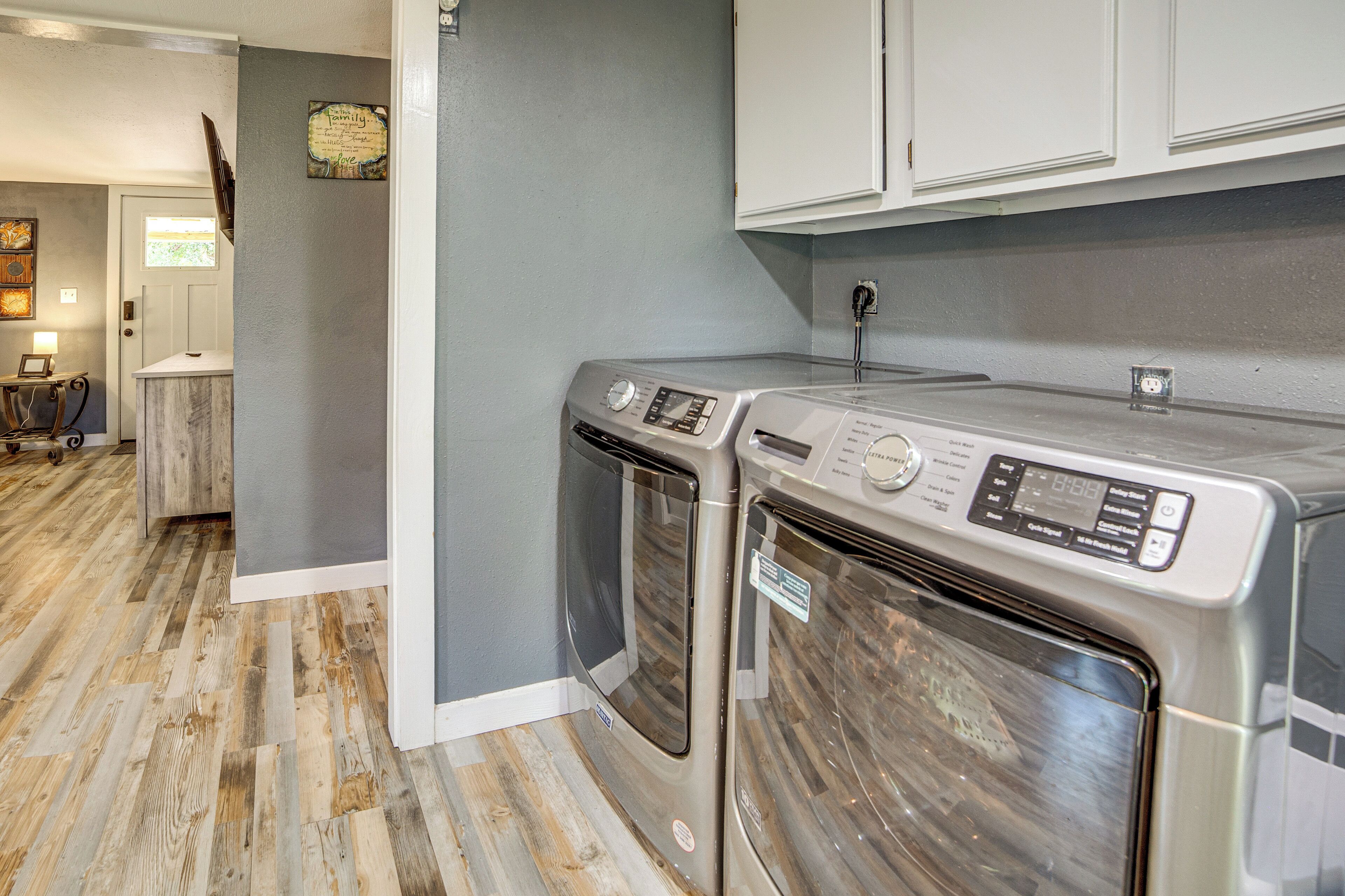 A laundry room with two front-loading washers and dryers, a wooden floor, and a gray wall.