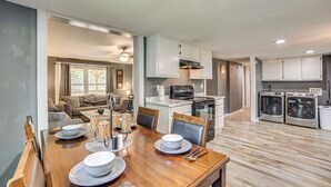 A modern kitchen with white cabinets, a dining area with a wooden table set for four, and a living room with a sofa and coffee table. - Lake Tawakoni Basecamp: Covered Patio + Fire Pit! (Wills Point)
