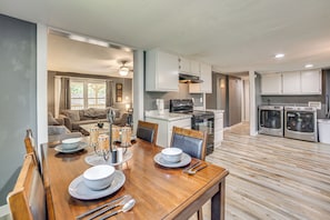 A modern kitchen with white cabinets, a dining area with a wooden table set for four, and a living room with a sofa and coffee table. - Lake Tawakoni Basecamp: Covered Patio + Fire Pit! (Wills Point)