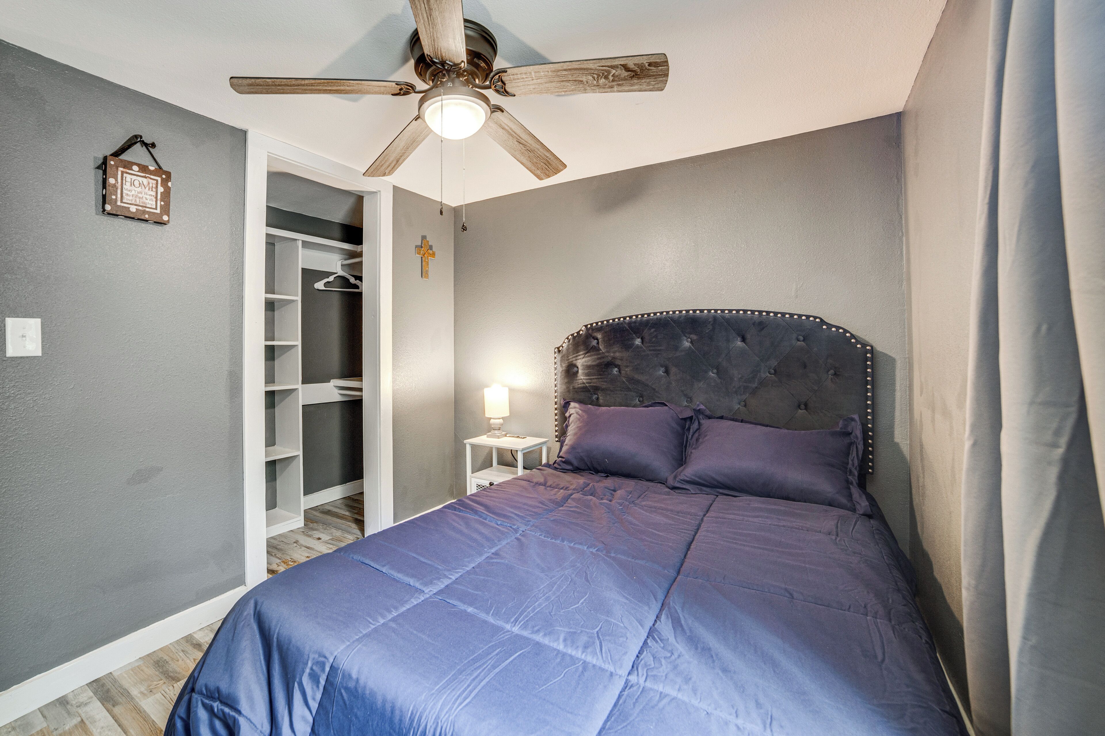 A bedroom with a bed, a ceiling fan, a nightstand, a closet, and a wall-mounted cross.