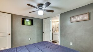 A bedroom with a bed, a ceiling fan, a television, and a door leading to a bathroom. - Lake Tawakoni Basecamp: Covered Patio + Fire Pit! (Wills Point)