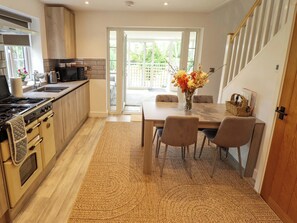 A modern kitchen with a stove, sink, and dining area with chairs and a table. - The Hen House (King's Lynn)
