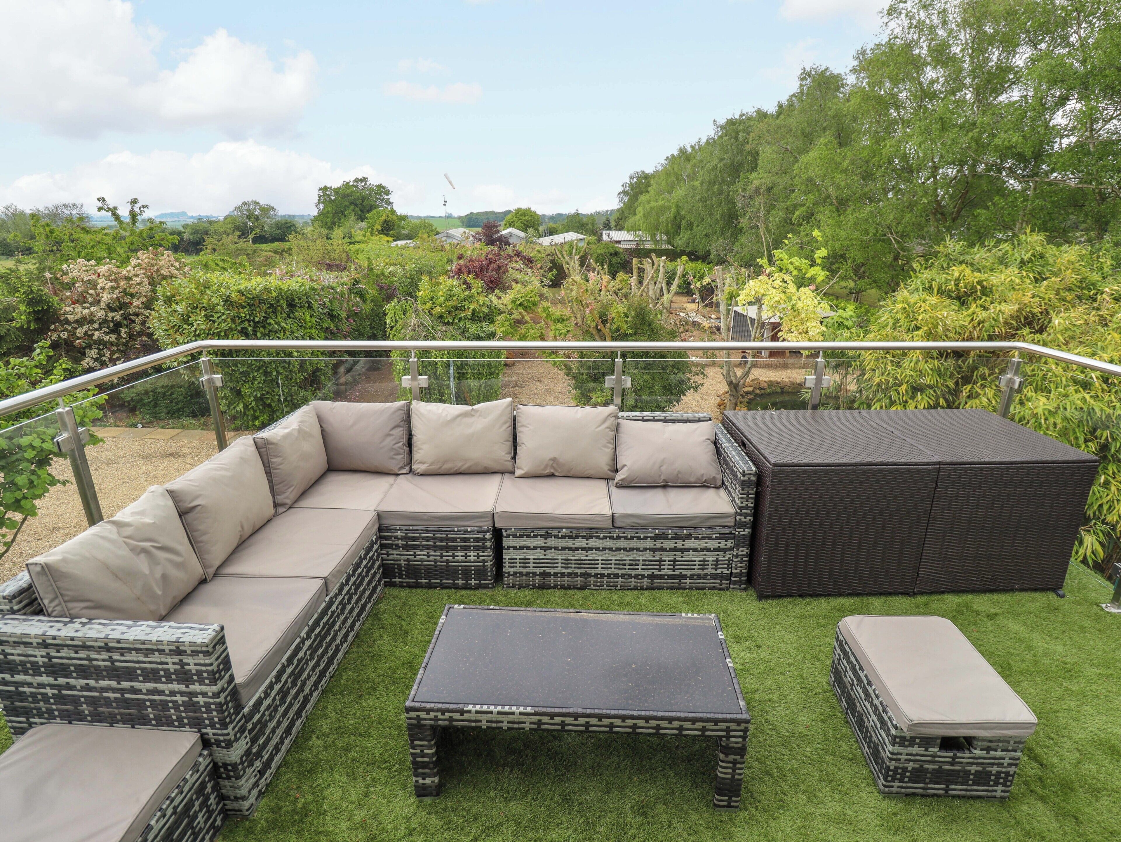 Een modulaire bank met kussens, een bijzettafeltje en een opbergkist op een balkon met een balustrade.