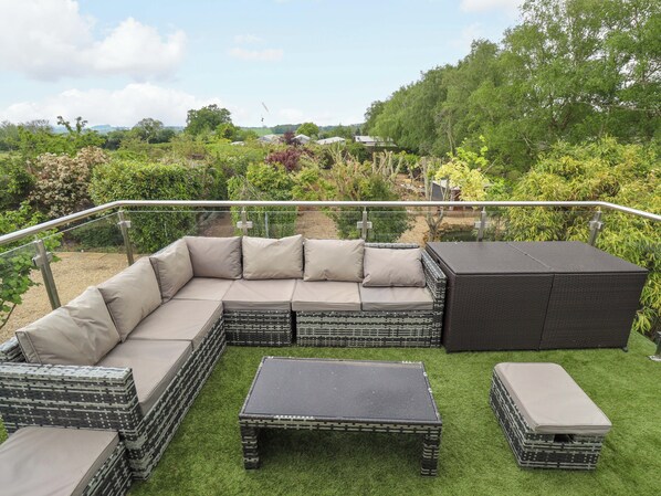 A sectional sofa with cushions, a small table, and a storage ottoman on a balcony with a railing. - The Hen House (King's Lynn)