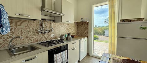 A compact kitchen with a gas stove, sink, and a view of the outdoors through a sliding door.