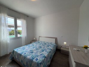 Ein Schlafzimmer mit Bett, Nachttisch, Lampe und einem Fenster mit Vorhängen.