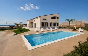 Ein modernes, zweistöckiges Gebäude mit Swimmingpool, weißen Liegestühlen und Meerblick.