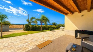 Eine Terrasse im Freien mit Holzboden, Grill und Blick auf den Strand.