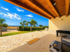 Eine Terrasse im Freien mit Holzboden, Grill und Blick auf den Strand.