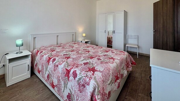 Ein Schlafzimmer mit Bett, Nachttisch, Schreibtisch, Stuhl, Kleiderschrank und Spiegel.